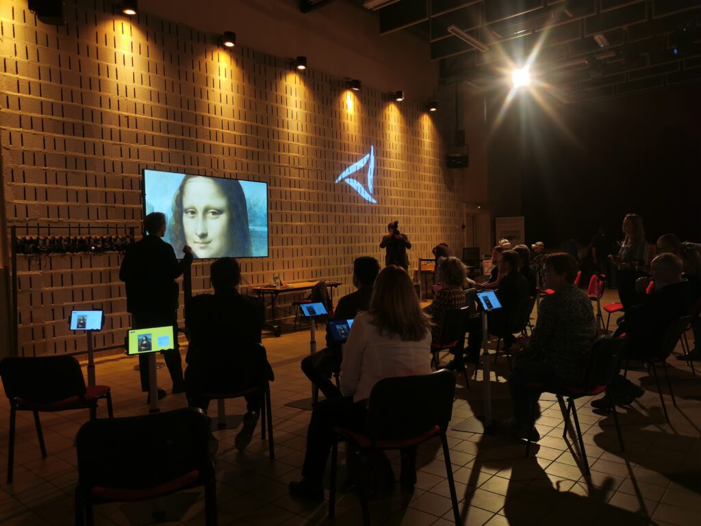 écran géant du musée numérique de l'espace Micro-Folie de Marines affichant le tableau de Léonard de Vinci "la Joconde", avec public assis utilisant des tablettes numériques